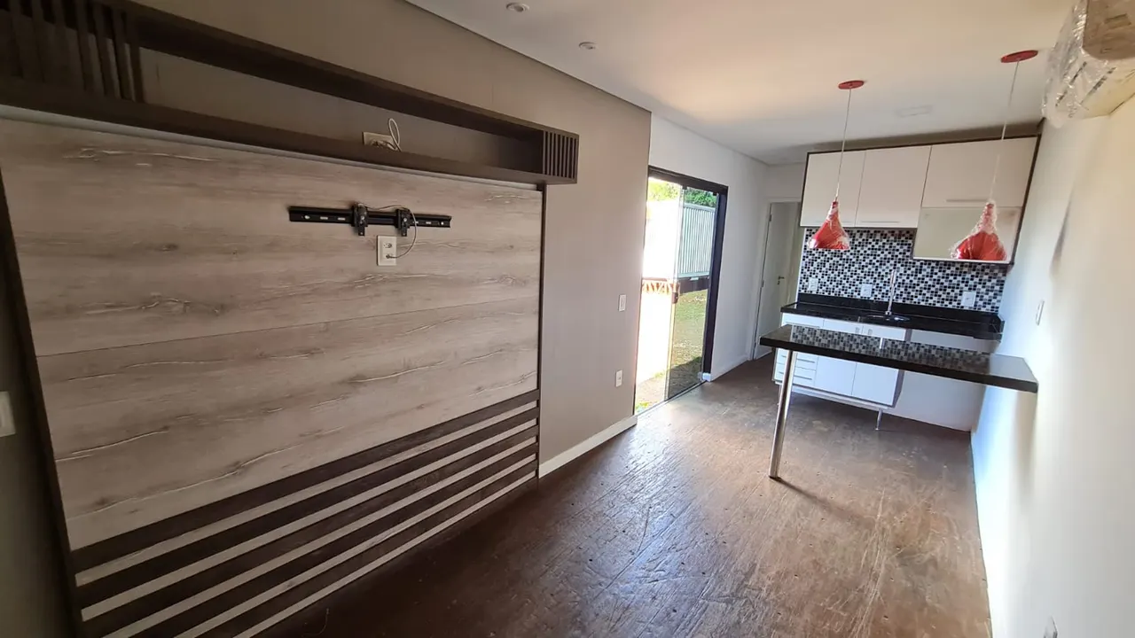 Sala do loft container de 30 m² com painel modular de madeira para TV, cozinha americana ao fundo e piso de compensado naval